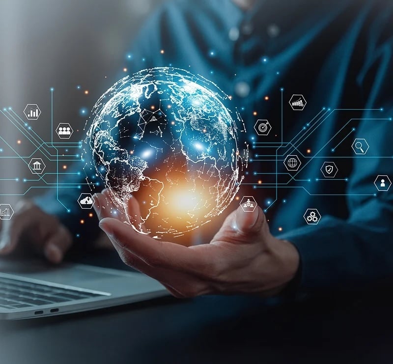 A person holds a digital globe with glowing blue and orange lights, symbolizing global technology connections, in front of a laptop.